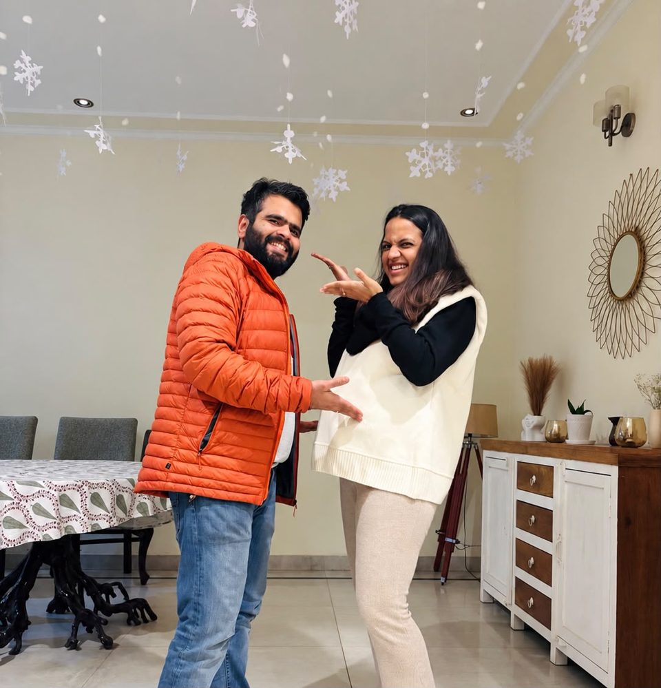 Surbhi and Manuj at home, laughing, with paper snowflakes hanging from the ceiling